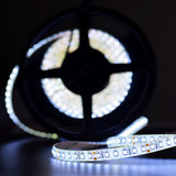 LYYT 24V LED strip light reel by AVSL illuminated in 6000K cool white, unspooled to show 2835 SMD LEDs on flexible white tape against a dark background.