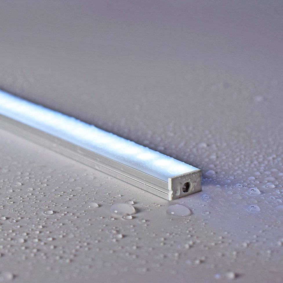 LYYT Waterproof Surface Mount LED Profile by AVSL, illuminated 1m aluminium channel with frosted diffuser on a water-droplet covered light grey surface.