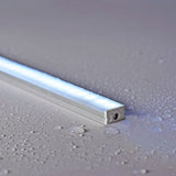 LYYT Waterproof Surface Mount LED Profile by AVSL, illuminated 1m aluminium channel with frosted diffuser on a water-droplet covered light grey surface.