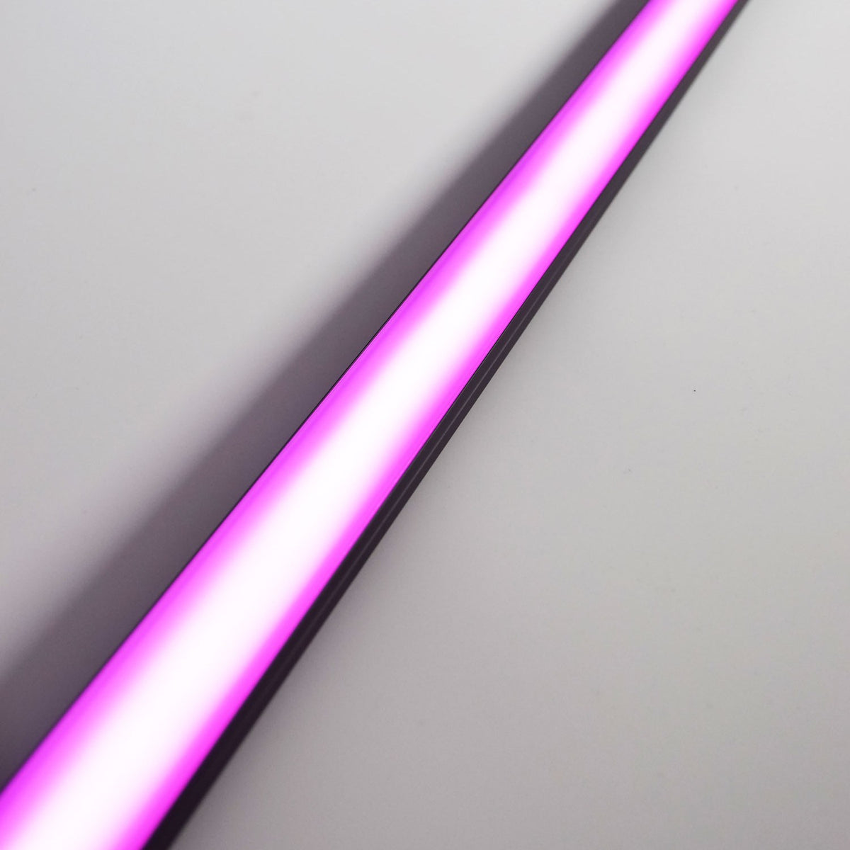 LYYT Tall Crown 1m black aluminium surface mount LED profile illuminated in pink, shown diagonally across a plain light grey background.