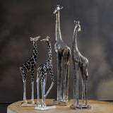 Libra Interiors Textured Electroplated Giraffe Sculptures in silver, four resin figures with black-recessed textured coats grouped on a wooden surface.
