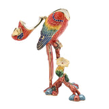 Macaw on Branch Metal Trinket Box in red with hinged beak lid, enamelled wings in yellow, green and blue, blue jewel accents, perched on a floral branch base, on a plain white background.