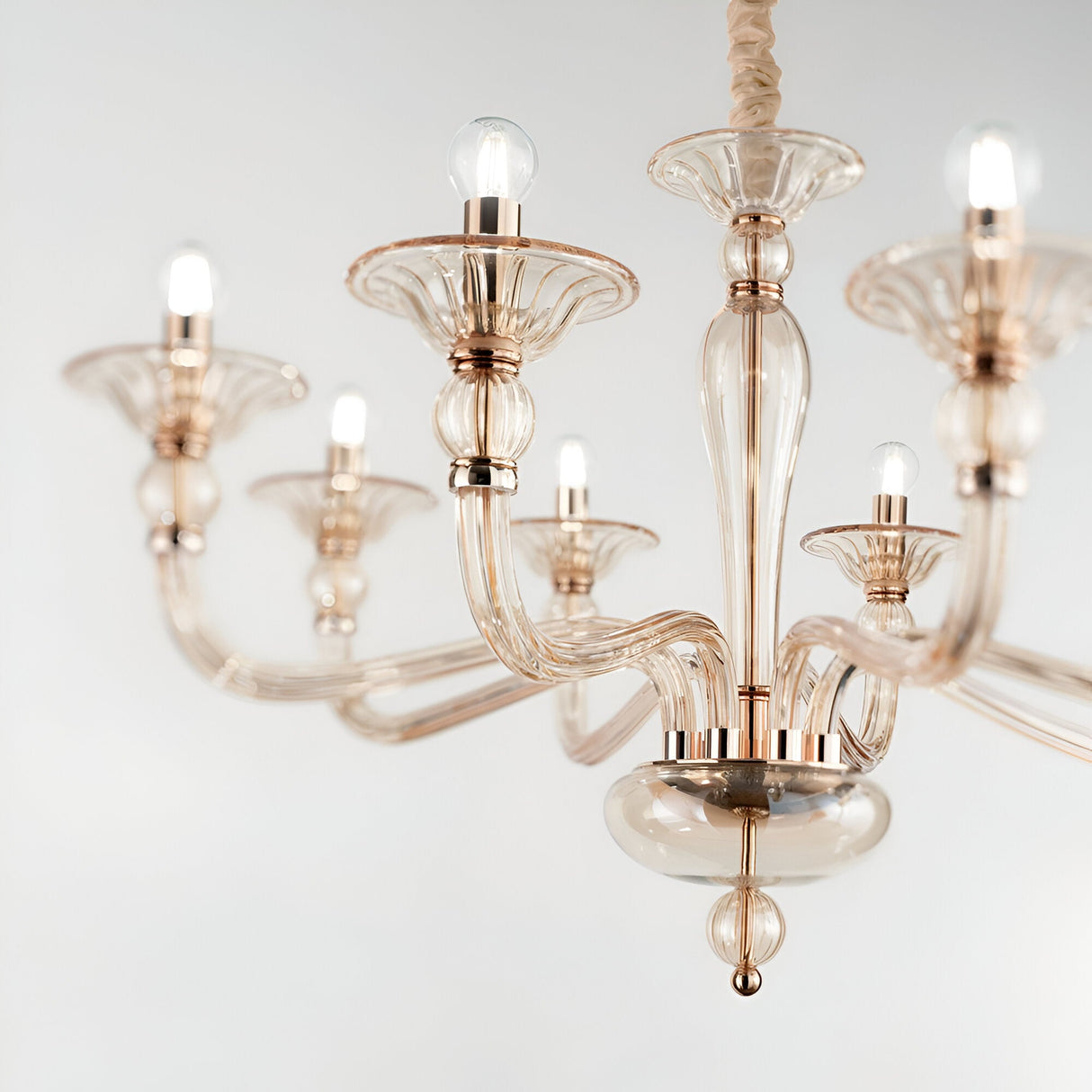 The Breeze Glass 8 Light Chandelier - Gold showcases an elegant design with eight curved arms, each supporting a glowing bulb. It features sleek glass shades and a polished gold finish, hanging gracefully from the ceiling against a neutral backdrop.