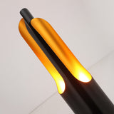 The Stealth Table Lamp - Brass & Black features a modern sculptural design with a sleek black and brass finish, glowing warm inner panels, and smooth curves—ideal for stylish contemporary lighting.