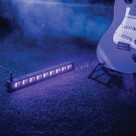 QTX UVB-9 UV LED Bar by AVSL, a black metal nine-LED 410nm ultraviolet fixture casting a violet glow across the floor beside an electric guitar in haze.