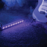 QTX UVB-9 UV LED bar by AVSL in a black metal housing with nine violet-lit LEDs, placed on carpet beside a white electric guitar amid haze.