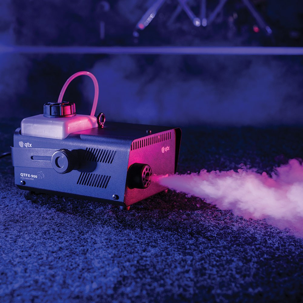 QTX QTFX-900 900W fog machine by AVSL in matt black housing with top-mounted fluid tank, emitting pink-lit fog across a stage floor.