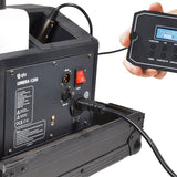 QTX UMBRA-1200 low mist generator rear panel showing DMX in/out XLR ports, red power switch, IEC inlet and detachable digital remote displaying Warming Up.
