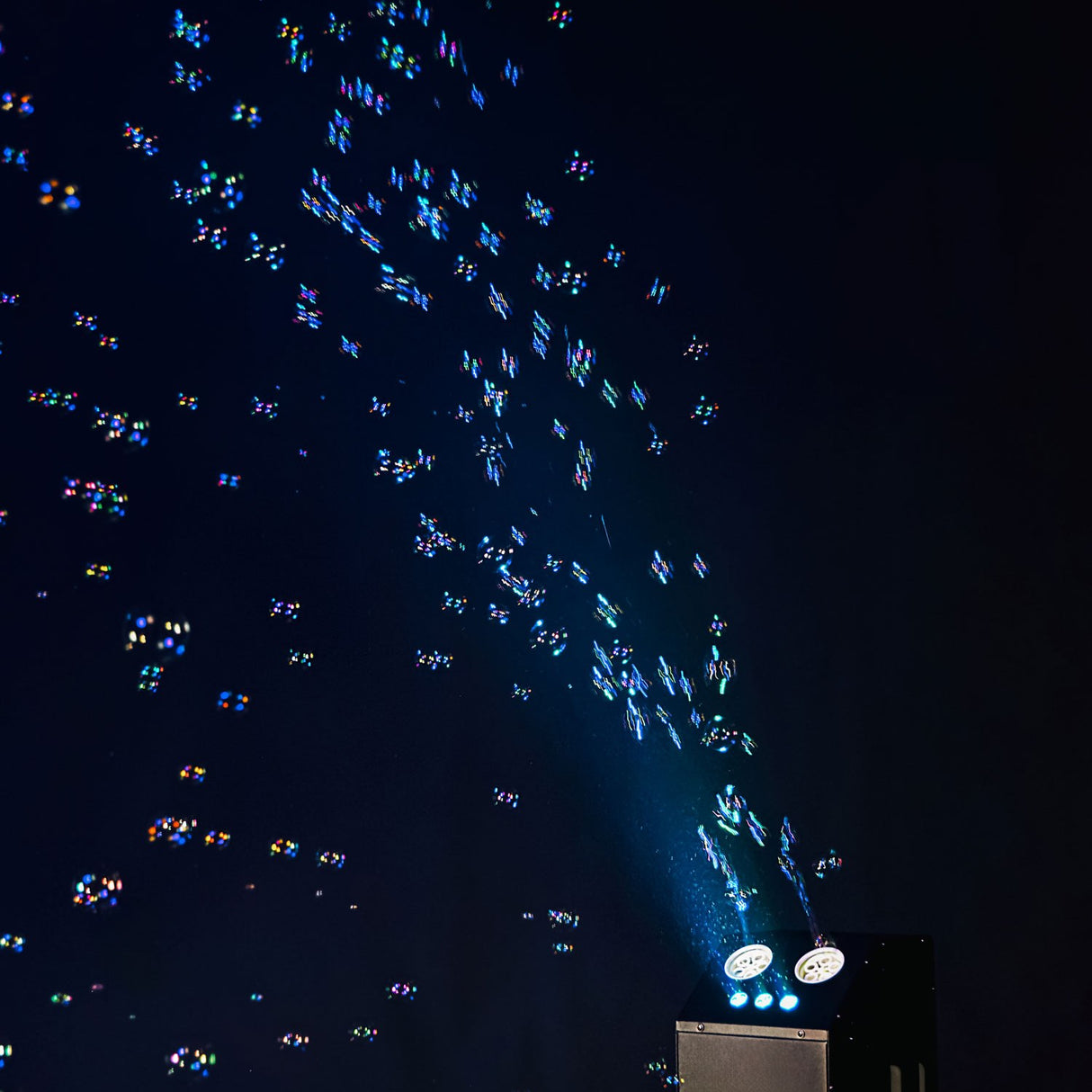 QTX Double Bubble LED RGB bubble machine projecting colourful illuminated bubbles from twin wheels into a dark room.