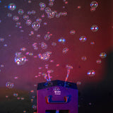 QTX Tetra Bubble machine in use, streaming bubbles upward from its four wheels against a dark red and purple lit background.