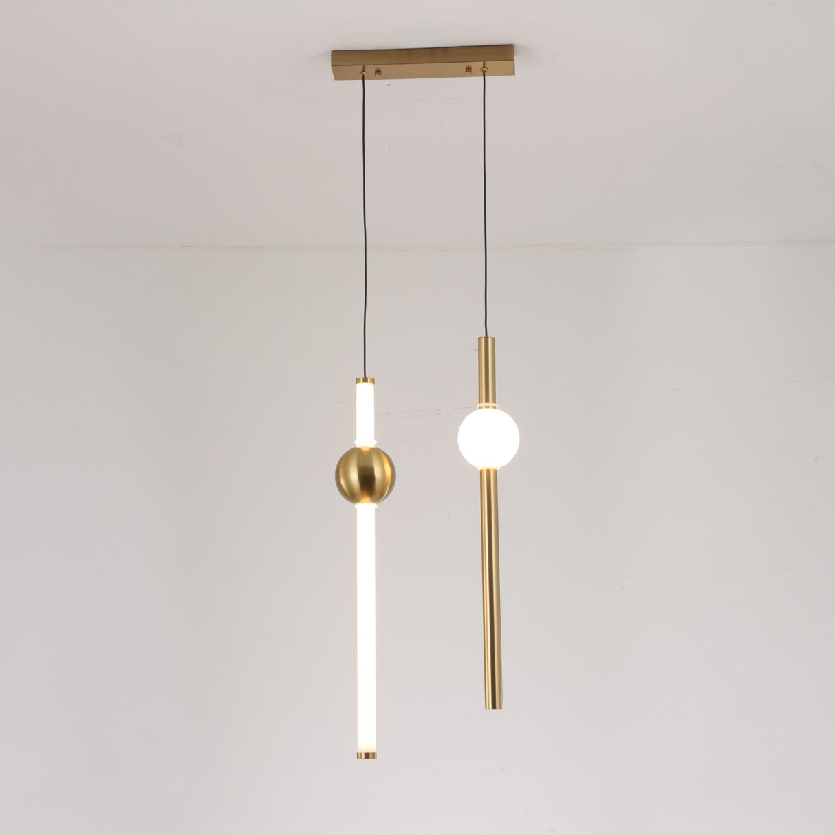 Two modern minimalist pendant lights with gold accents hang from the ceiling: one is the Sottile LED Vertical Suspension Light - Gold, featuring a frosted tube and gold sphere; the other has a vertical gold rod with a round white bulb.