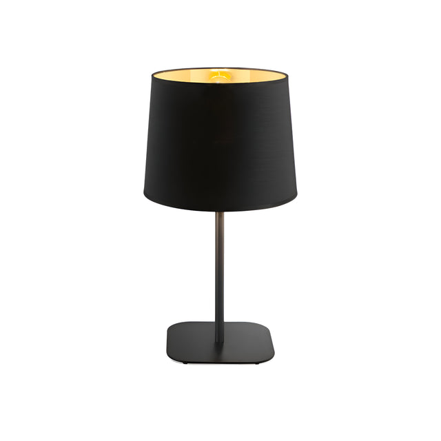 The Hive Table Lamp in black, featuring a sleek cylindrical shade and a slim, straight base, rests gracefully on a flat surface. Its illuminated shade casts a soft glow that highlights its minimalist design, making it an elegant addition to any home's decor.