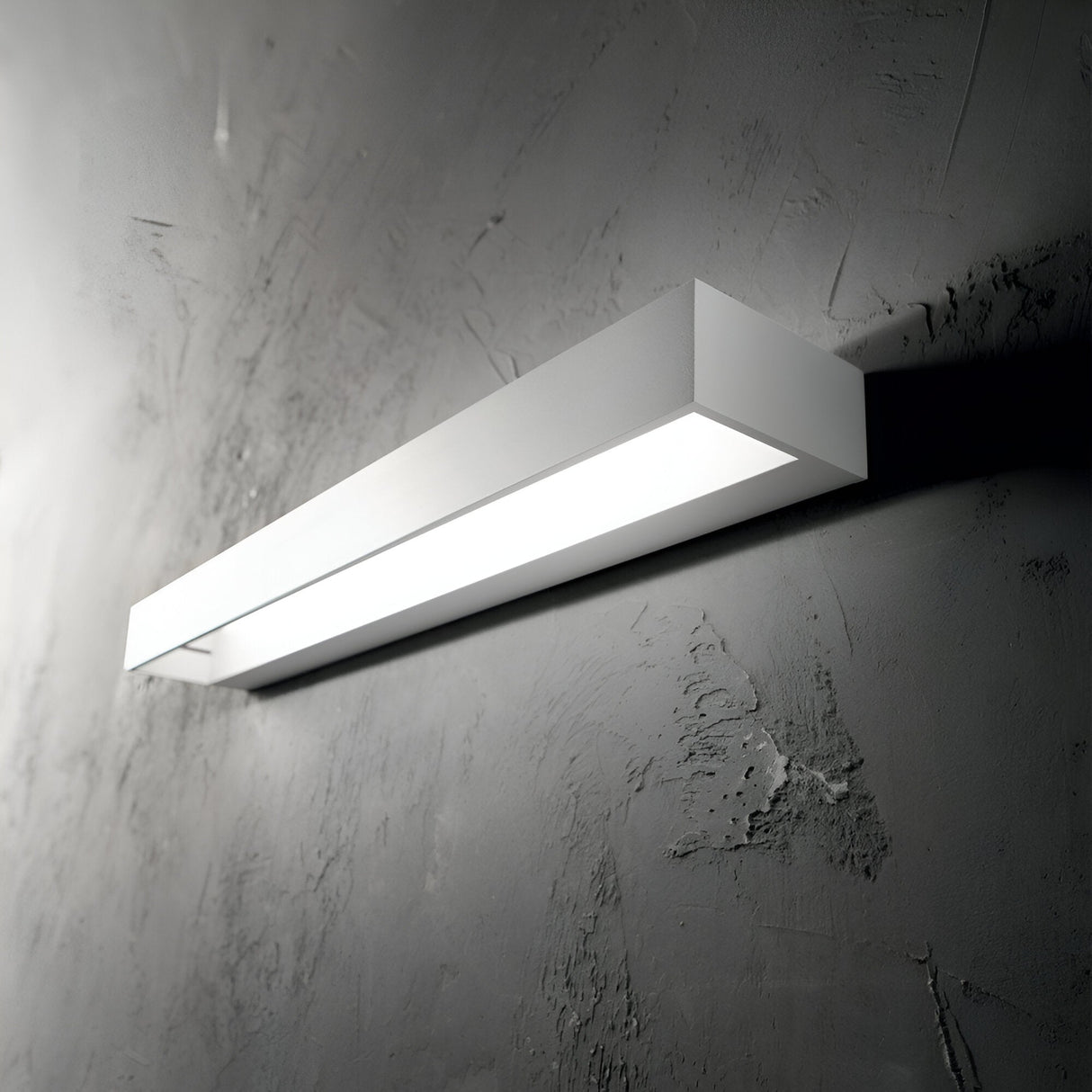 The Quantum LED Wall Light 8W 3000K - White, measuring 60cm in length, features a minimalist rectangular design and is mounted on a textured gray wall to provide a modern touch. It delivers soft, even illumination downward while maintaining energy efficiency.