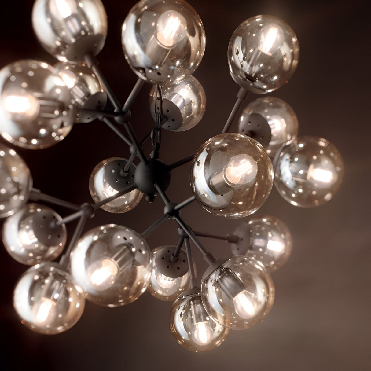 A close-up of the Novara 18 Light Chandelier in black showcases its modern design, featuring multiple spherical glass bulbs arranged in a cluster that emit warm light. This fixture exudes contemporary charm against a dim background, creating a cozy ambiance.