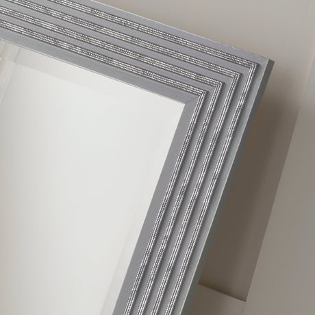 Close-up of the Pearl Rectangle Wall Mirror in grey/silver, showcasing its rectangular shape with a silver beaded frame and four parallel lines. This elegant piece graces a light-colored wall, reflecting a minimalistic home decor design.