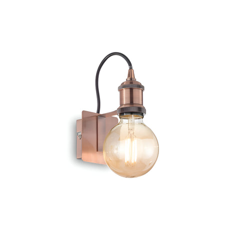 The Zip Wall Light - Copper is a wall-mounted fixture featuring a large, round Edison bulb that showcases an exposed design with visible filaments. This piece connects to the metal base with a black cord, embodying an industrial design and vintage aesthetic that brings timeless charm to any space.