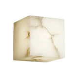The Calmora 1 Light Block Alabaster Wall Light - Soft White is a cube-shaped fixture crafted from natural Spanish alabaster, showcasing translucent surfaces with gentle brownish veins and cracks against a white background.