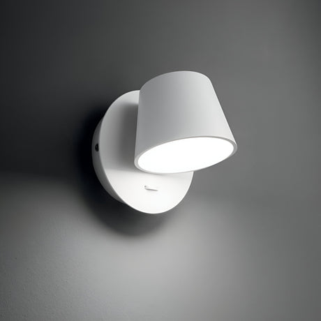 The Gim LED Wall Light 6W 3000K - White, featuring a modern, minimalist design with a circular base and cylindrical shade, is mounted on a gray wall in contemporary interiors. When switched on, this energy-efficient lamp casts a soft, diffused glow.