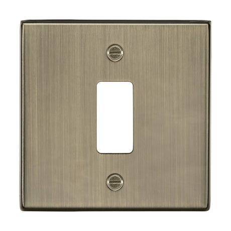 The 1 Gang Grid Faceplate in Antique Brass, crafted for the Knightsbridge Grid System, boasts a rectangular opening with a brushed finish and two visible screws for mounting.