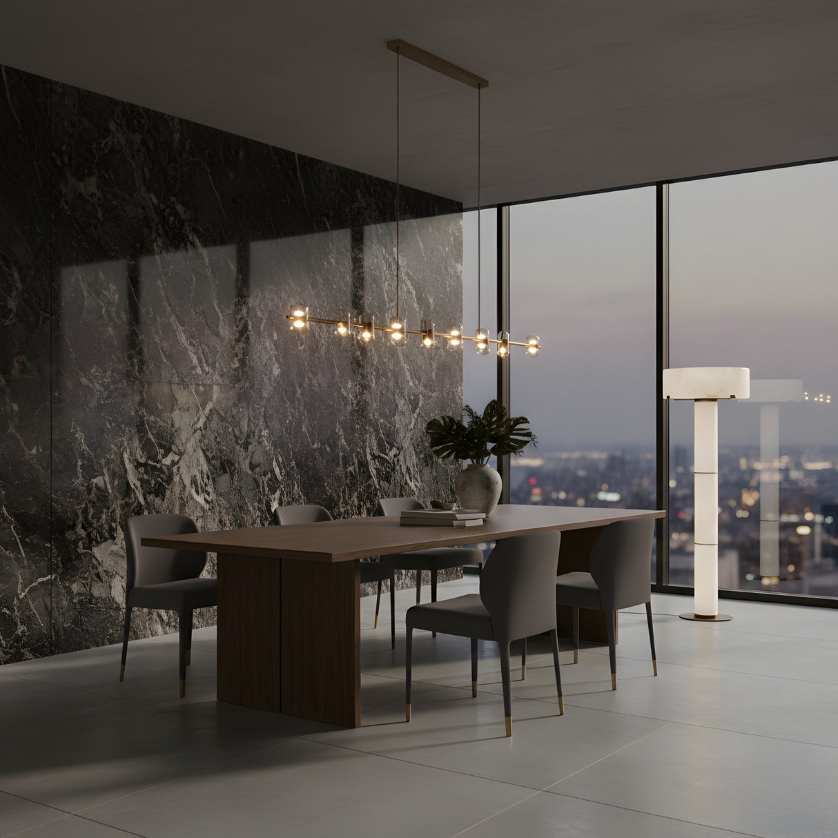 A modern dining room features a wooden table, six gray chairs, a marble accent wall, large city-view window at dusk, a contemporary chandelier, and the Virex 3 Light Tiered Column Alabaster Floor Lamp – Soft White. A vase with leaves sits on the table.