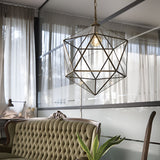 The stylish room features the Verdant 1 Light Large Pendant in a brass finish, hanging from the ceiling amidst frosted glass panels. Positioned below is a green tufted sofa, complemented by a plant placed to the right. Soft natural light gently filters through sheer curtains that cover the expansive windows.