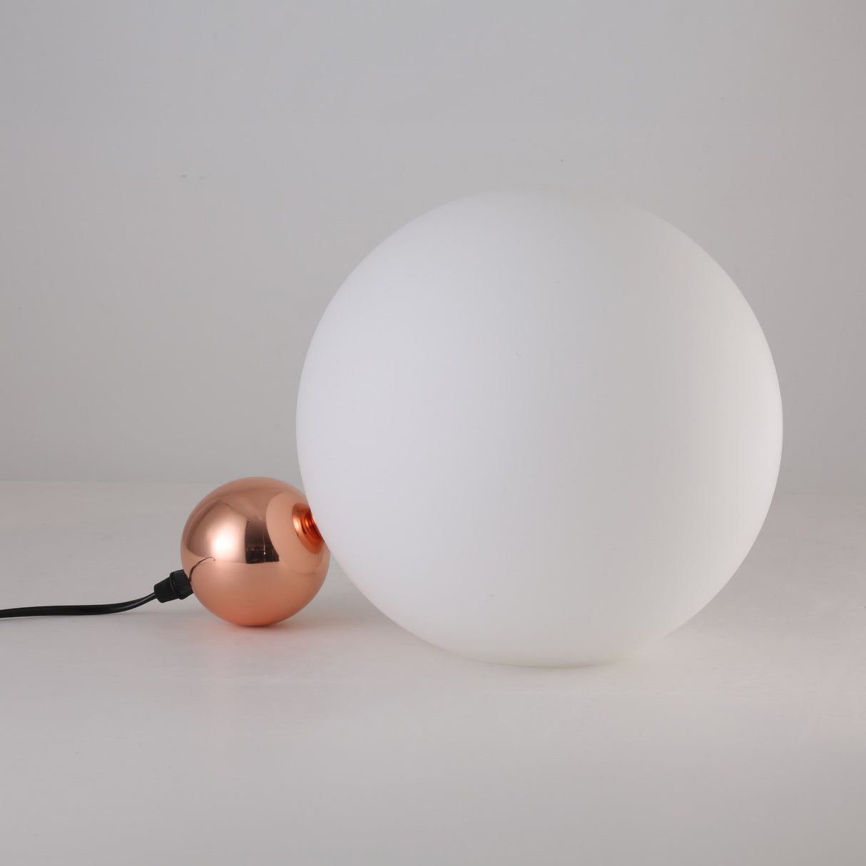 The Soul Table Lamp - Copper showcases a large white frosted glass globe on a sleek copper sphere base with a black power cord, all set against a plain white background.