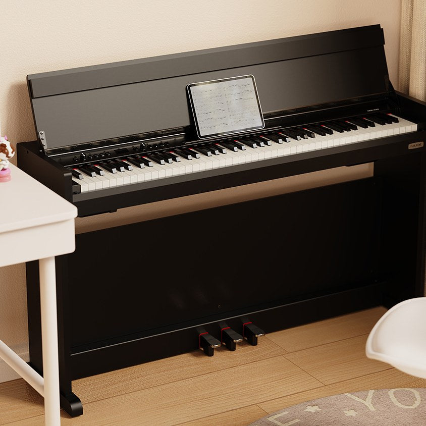 NU-X NCK-330 88-note weighted digital upright piano in black gloss with three pedals and tablet displaying sheet music on the stand, in a home setting.
