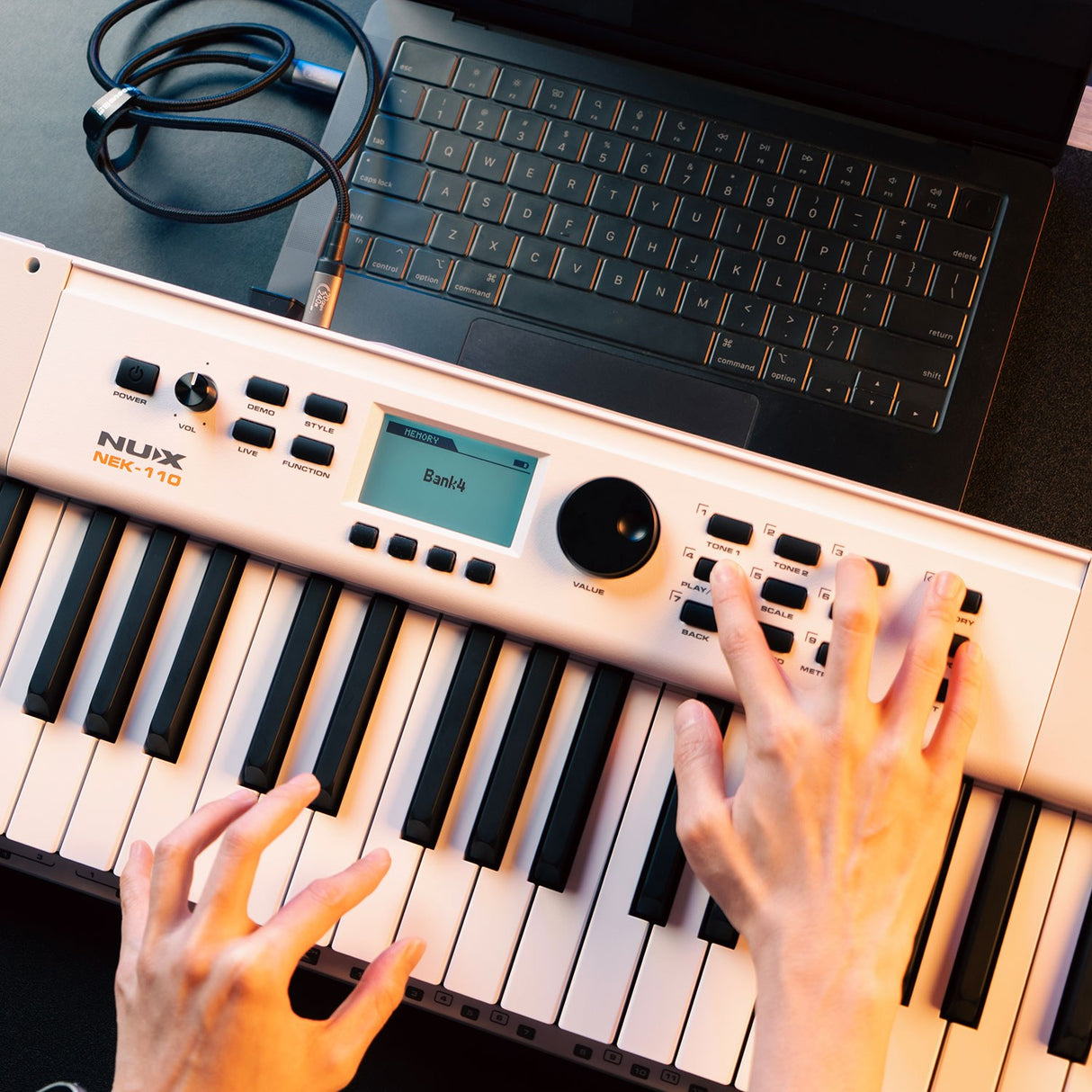 Hands playing the NU-X NEK-110 61-key portable keyboard in white, shown beside a laptop with USB cable connected in a desktop setup.