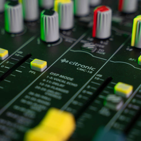 Close-up of the Citronic CMC-18 mixing console showing green and red knobs, yellow PFL buttons, channel faders and DSP mode labelling.