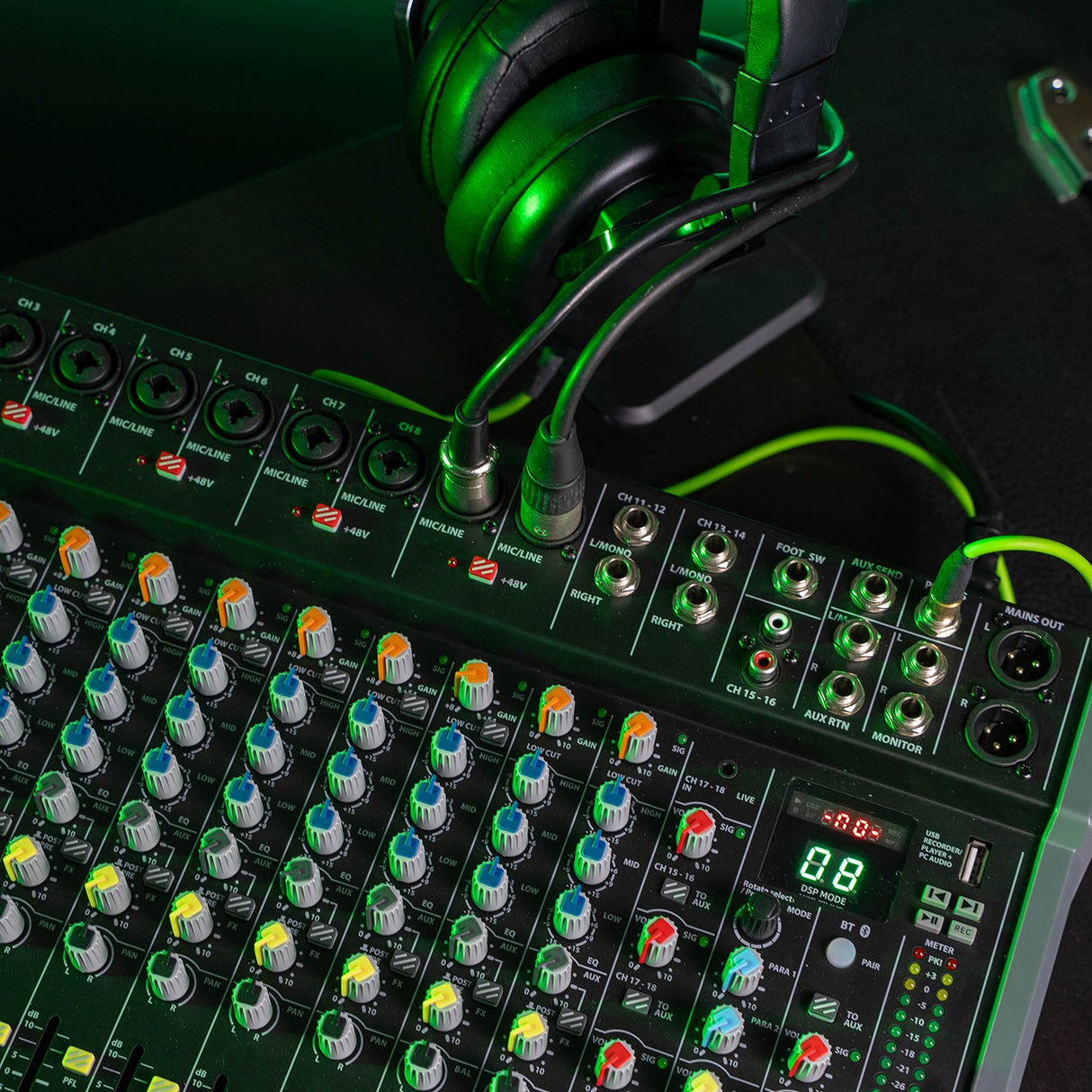 Citronic CMC-18 live mixing console with multiple mic/line inputs, EQ knobs, DSP display and USB port, shown with green-lit headphones resting above.