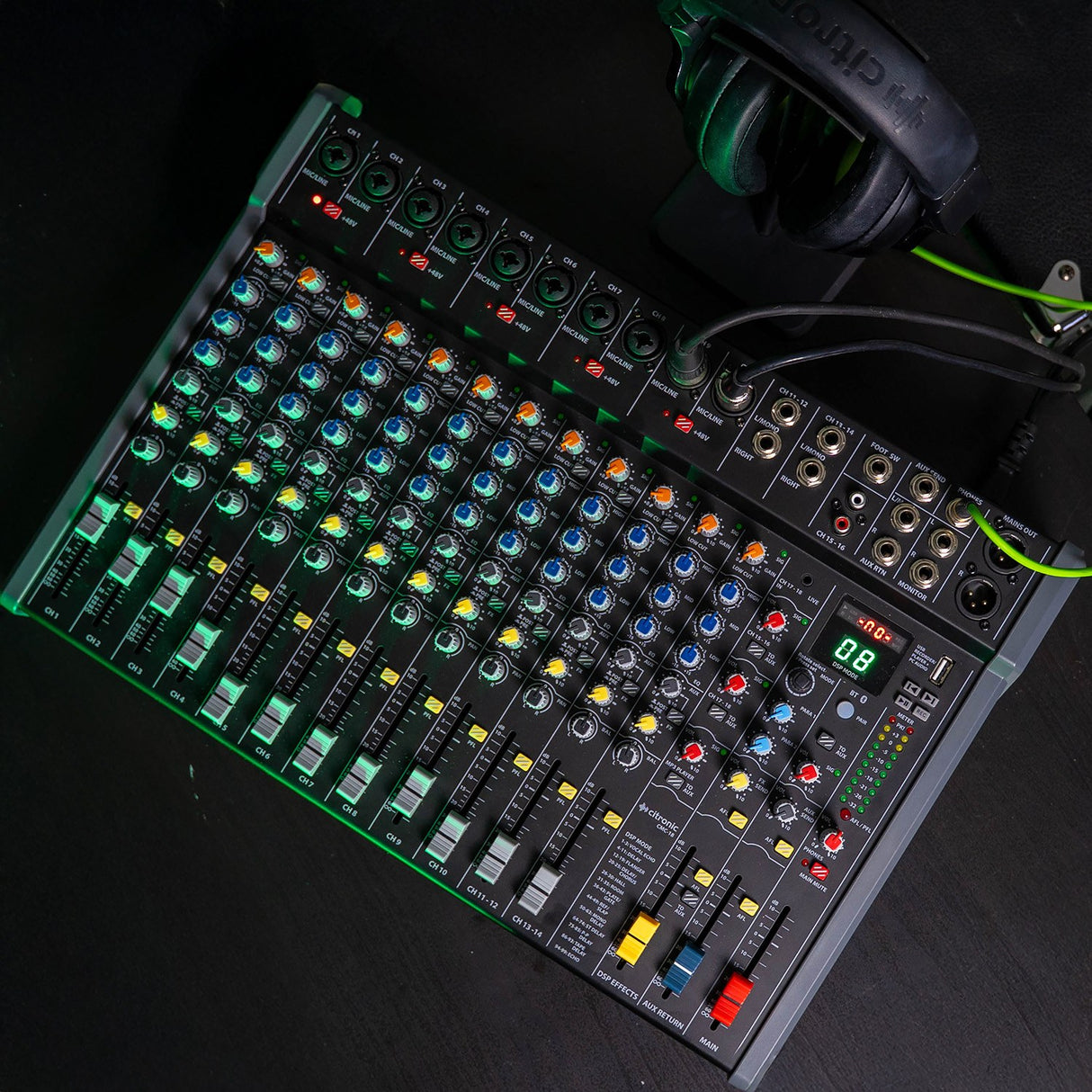 Citronic CMC-18 live mixing console with multiple channel faders, EQ knobs, DSP display and USB port, shown on a dark surface with headphones.