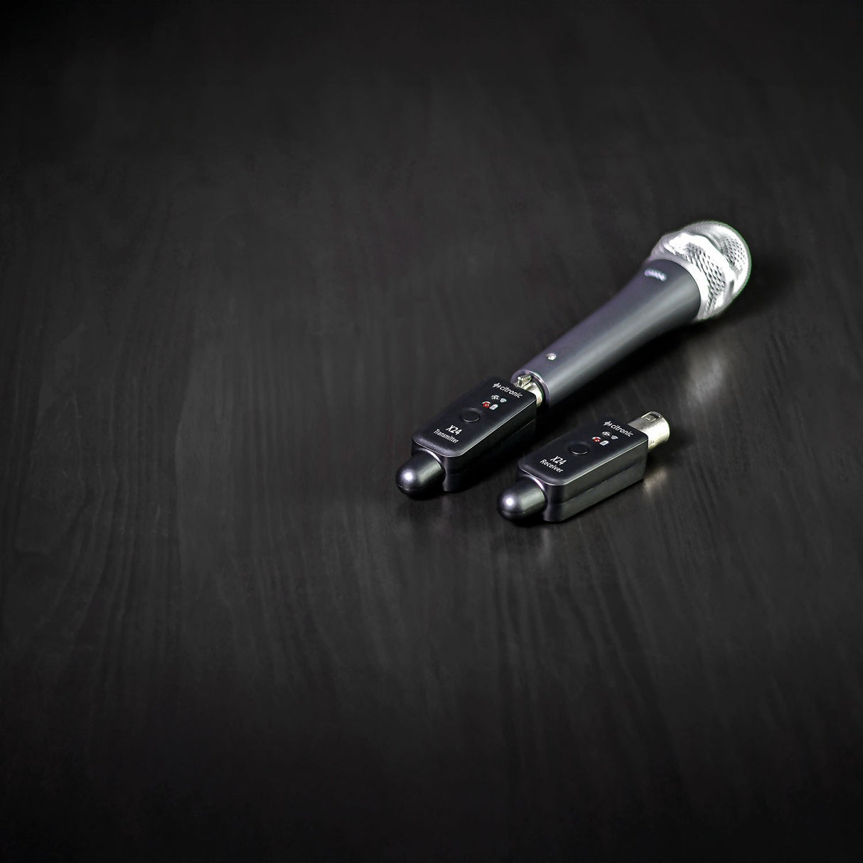 Citronic X24 2.4GHz wireless XLR transmitter and receiver plugged into a handheld dynamic microphone on a dark wood surface.