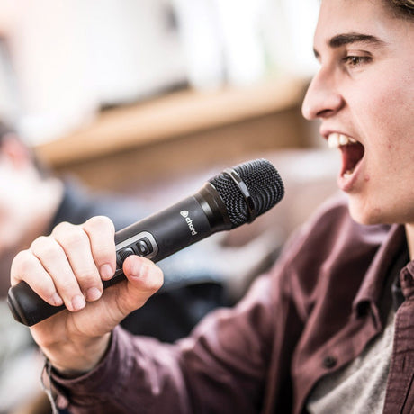 Man singing into a Chord NUHH-863.1 handheld wireless microphone transmitter in matte black, holding the dynamic mic close to his mouth indoors.