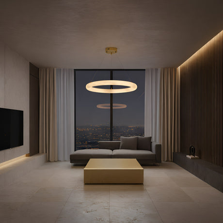 A modern living room at night showcases a gray sectional, square coffee table, wall-mounted TV, large city-view window, and minimalist decor. The space is softly lit by the Seraphis LED Small Alabaster Chandelier in Soft White.