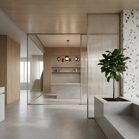 A modern, minimalist interior with light wood accents, terrazzo wall, large potted plant, and a sleek kitchen island highlighted by the Petal 8 Light Chandelier - Copper. Natural light pours in from expansive windows behind.