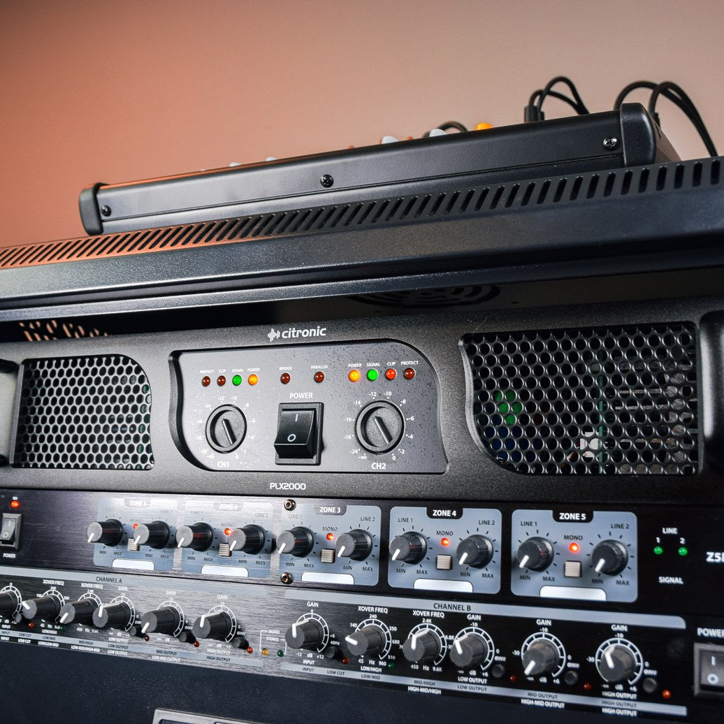 Citronic PLX2000 2U rackmount power amplifier installed in a rack, showing front panel with dual channel level knobs, power switch and LED indicators.