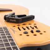 Cherub CGC-1 Gemini adjustable guitar capo in matte black resting on a natural wood Godin guitar body with visible control buttons.