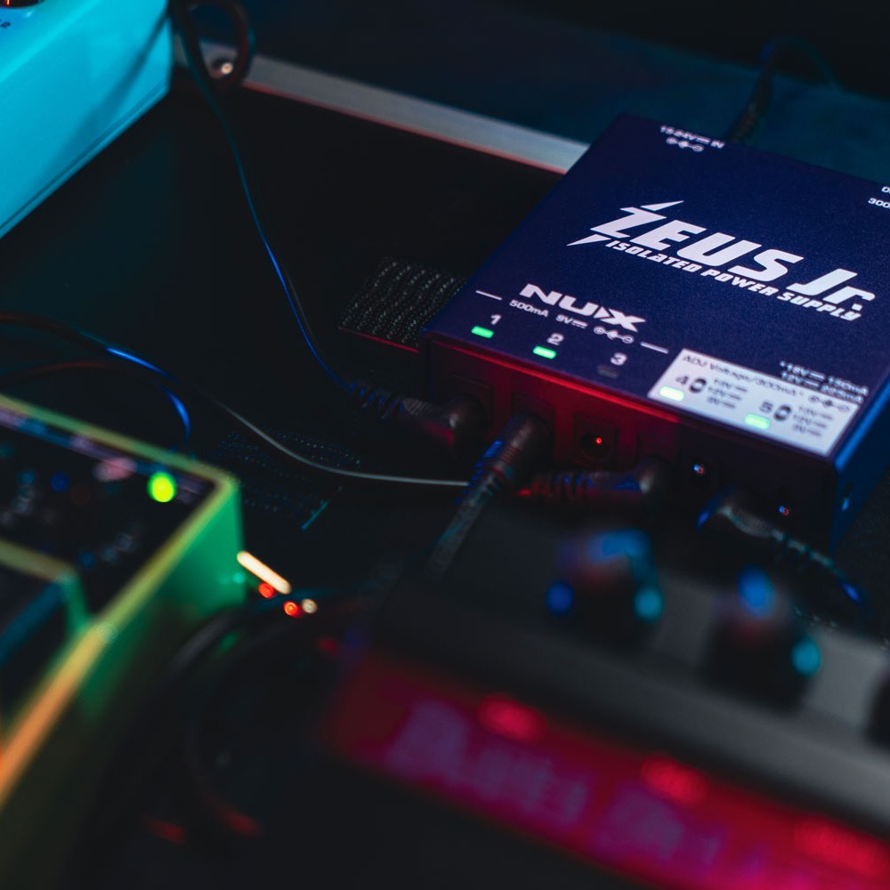 NU-X NIP-Z6 Zeus Jr. Isolated Pedal Power Supply in blue casing with lit output indicators, connected to pedals on a board under coloured lighting.