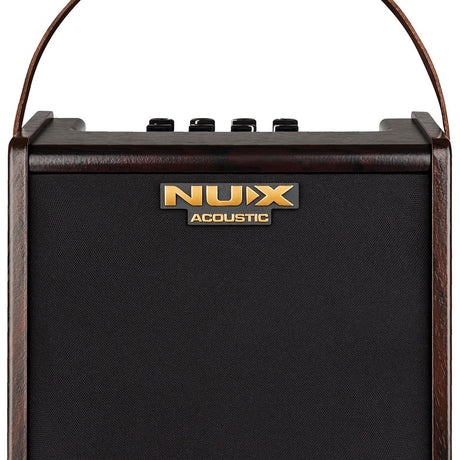 NU-X AC-25 portable acoustic guitar amp with wood-effect cabinet, black grille, gold Acoustic badge, top control knobs and leather carry strap.