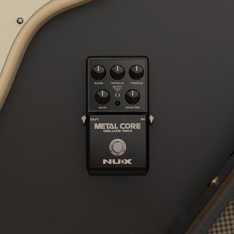 NU-X Metal Core Deluxe mkII distortion pedal in matte black with Bass, Middle, Treble, Gain, Master knobs and model switch, mounted on a guitar amp.