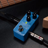 NU-X NDL-3 Hook Drum Machine and Looper Pedal in blue with three black knobs, footswitch and connected jack cables beside a guitar neck.