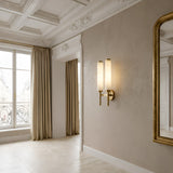 Elegant room with tall windows, beige curtains, wall molding, and a gold-framed mirror. The Noctera LED Twin Column Alabaster Wall Light in Soft White & Brushed Brass casts a warm glow on the neutral walls.