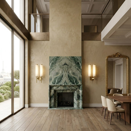 A modern living room featuring tall windows, a green marble fireplace, ornate mirror, wooden dining table with cream chairs, and Noctera LED Twin Column Alabaster Wall Lights in brushed brass; the Eiffel Tower visible outside.