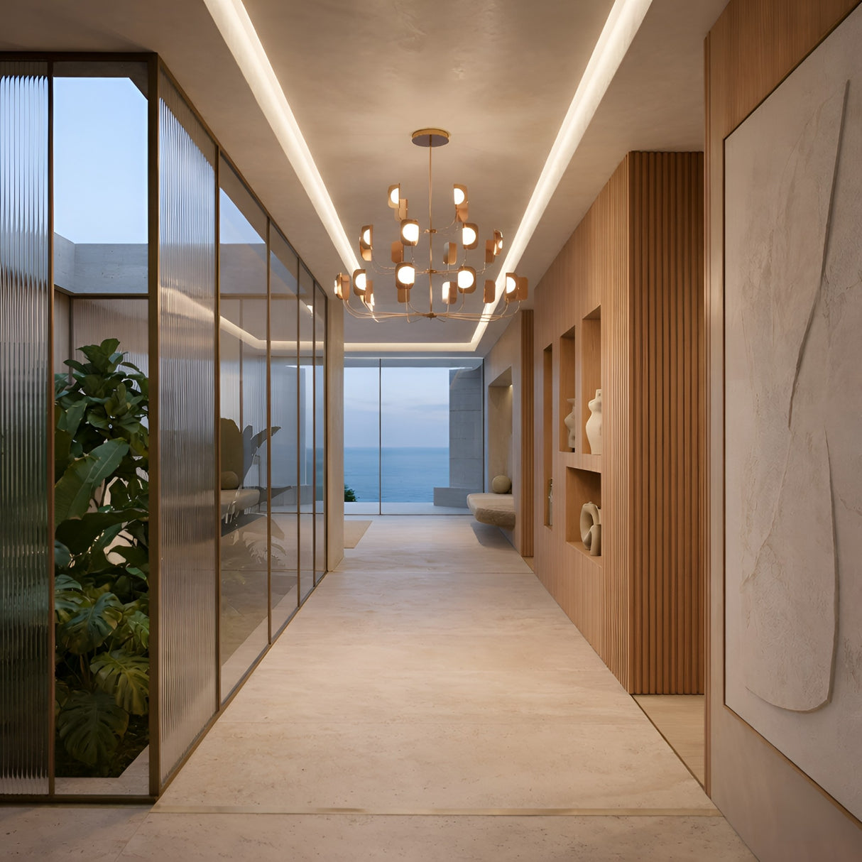 A modern hallway with beige floors, wood panel walls, built-in shelves, a Petal 24 Light Chandelier - Copper for luxury lighting, glass panels showing greenery, and large windows with ocean and sky views.