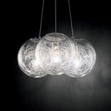 The Lyria 3 Light Cluster Pendant in silver showcases three clear blown glass diffusers, each enveloped by a decorative wire network surrounding a bulb. This elegant cluster pendant emits a soft, warm glow against a dark background, adding sophistication to any modern design lighting atmosphere.