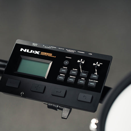 Close-up of the NU-X DM-310H digital drum module in matte black, showing the backlit display, tone and click buttons, reverb and kit dials, and rear ports.