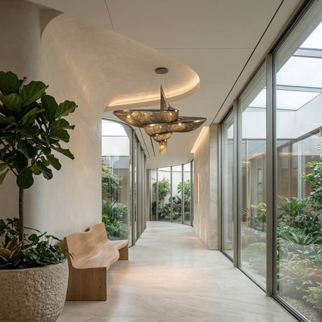 A modern hallway features a sculptural wooden bench, large indoor plant, and floor-to-ceiling windows. Curved walls and the Stratiform 20 Light Metal Chain Veil Chandelier in Champagne create a tranquil, contemporary atmosphere.