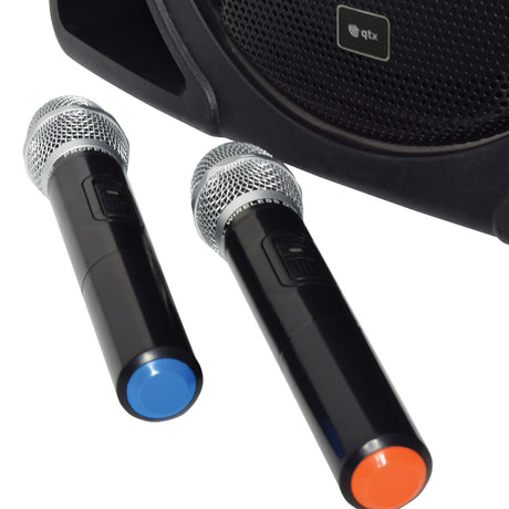 Close-up of the QTX DELTA-200 portable PA system's black speaker grille with two included UHF wireless handheld microphones with blue and orange tips.
