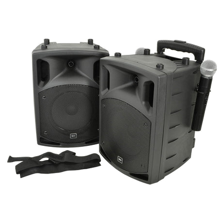 Two black QTX PAV8 portable speakers with a curved design are shown side by side. One speaker includes an attached UHF microphone, featuring a handle above and two straps lying in front, all components of this efficient portable PA system.