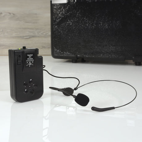 QTX BHS-174.1 VHF beltpack transmitter in black with on switch and headset microphone on a boom, shown beside a portable PA unit.